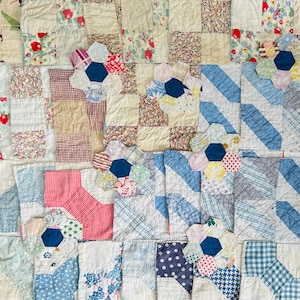 May include: A patchwork quilt featuring a variety of fabric squares in floral, gingham, plaid, and polka dot patterns. The quilt includes several hexagonal flower-shaped appliqués in shades of blue, red, yellow, and white stitched onto the surface.