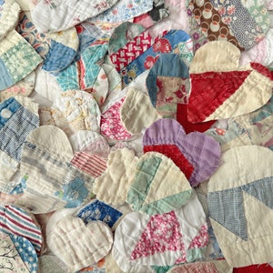 May include: Close-up of a patchwork quilt composed of numerous heart-shaped fabric pieces. The hearts are made from various patterned fabrics in shades of red, blue, pink, and white. The quilt's design is a mix of textures and patterns, creating a vintage aesthetic.