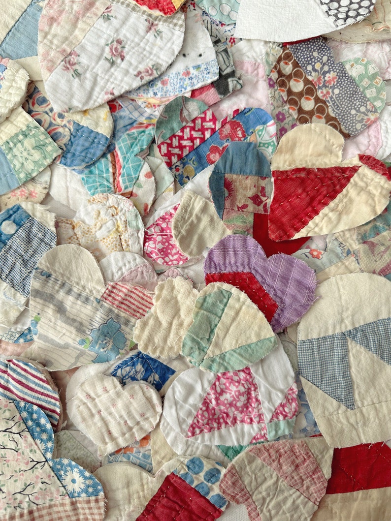 May include: Close-up of a patchwork quilt composed of numerous heart-shaped fabric pieces. The hearts are made from various patterned fabrics in shades of red, blue, pink, and white. The quilt's design is a mix of textures and patterns, creating a vintage aesthetic.