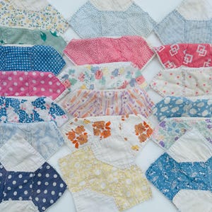 May include: A collection of colorful, vintage fabric patches. The patches feature various patterns, including polka dots, floral prints, and geometric designs. The color palette includes pink, blue, yellow, and orange. The patches are arranged in a grid-like pattern.