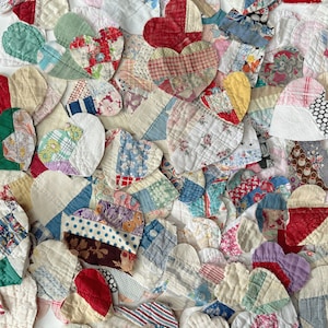 May include: A close-up view of a collection of heart-shaped fabric patches in various colors and patterns. The patches are made from different fabrics, including floral prints, stripes, and solid colors. The hearts are arranged closely together, creating a textured and colorful display.