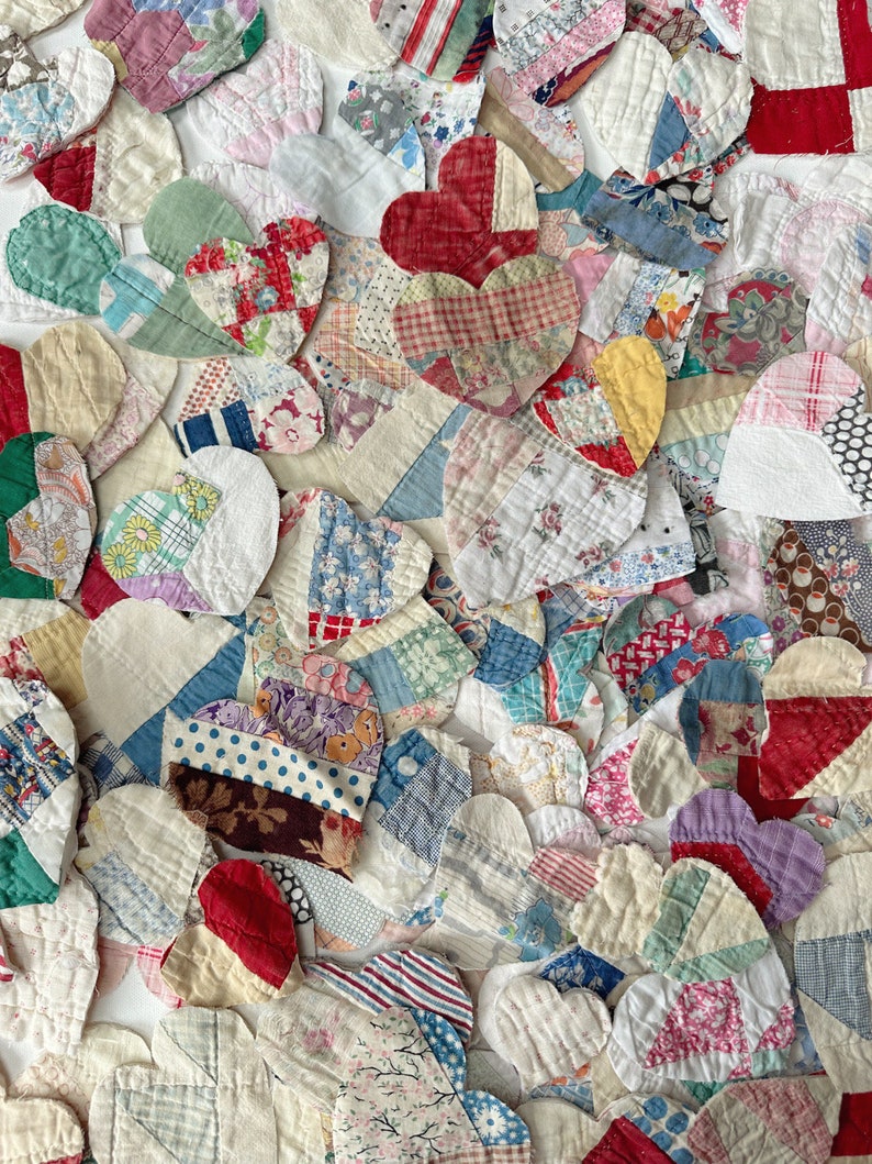 May include: A close-up view of a collection of heart-shaped fabric patches in various colors and patterns. The patches are made from different fabrics, including floral prints, stripes, and solid colors. The hearts are arranged closely together, creating a textured and colorful display.
