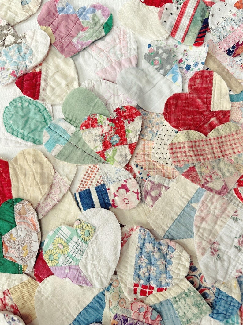 May include: A collection of handmade fabric hearts in various sizes and patterns. The hearts are made from a variety of fabrics, including floral prints, stripes, and solid colors. The color palette includes red, pink, blue, green, and white.