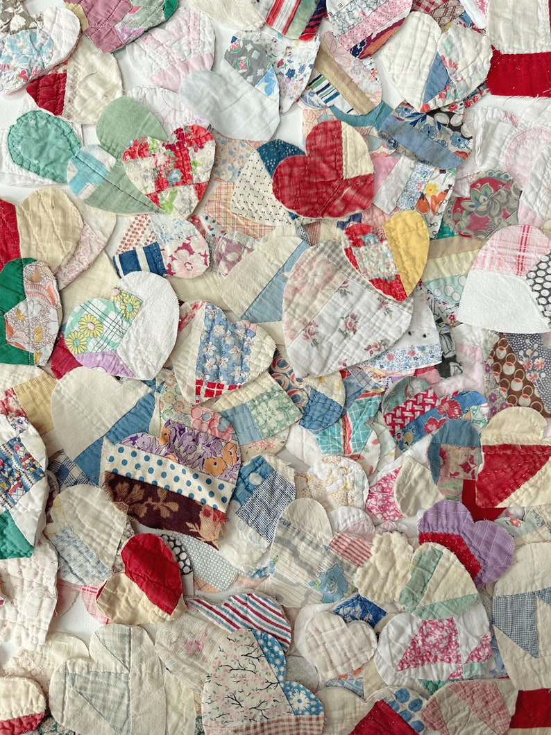 May include: A collection of heart-shaped fabric patches in various colors and patterns. The patchwork includes floral, striped, and solid fabrics in shades of red, blue, green, and white. The hearts are arranged closely together, creating a textured surface.