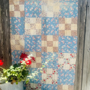 May include: A patchwork quilt featuring a repeating grid pattern of alternating squares. The design consists of light blue fabric squares with a small floral print and cream-colored squares with a dense, multi-colored floral pattern throughout.