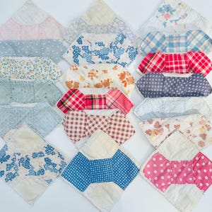 May include: A collection of vintage fabric bibs in various patterns and colors. The bibs feature floral, plaid, polka dot, and striped designs in shades of blue, red, pink, and cream. Each bib has a unique shape and is made of soft, quilted fabric.