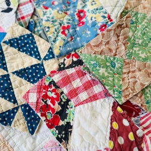 May include: A patchwork quilt composed of various fabric squares featuring diverse patterns including red and white gingham, blue and white stars, floral prints in red, yellow, and green, and striped textiles, all joined with visible quilting stitches.
