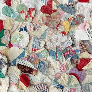 May include: A collection of handmade fabric hearts in various sizes and patterns. The hearts are made from a patchwork of vintage fabrics in shades of red, blue, white, and yellow. The overall effect is a charming, handcrafted aesthetic.
