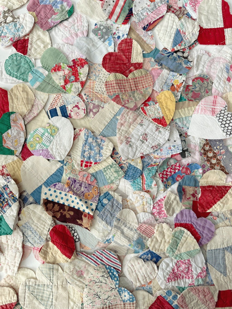 May include: A collection of handmade fabric hearts in various sizes and patterns. The hearts are made from a patchwork of vintage fabrics in shades of red, blue, white, and yellow. The overall effect is a charming, handcrafted aesthetic.