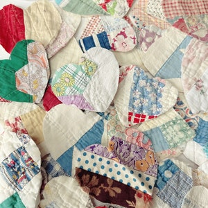 May include: A collection of heart-shaped fabric patches in various colors and patterns. The patches include floral prints, polka dots, and solid colors, creating a patchwork design. The hearts are arranged closely together, showcasing a handmade, vintage aesthetic.