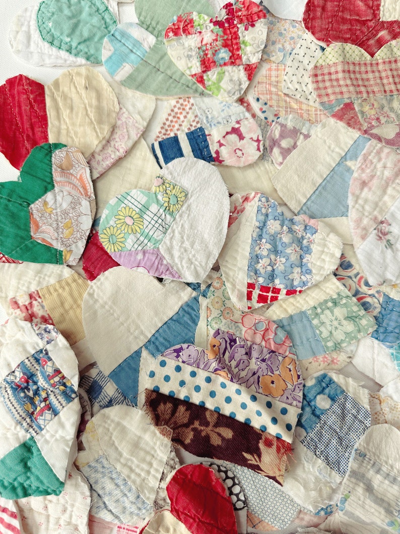 May include: A collection of heart-shaped fabric patches in various colors and patterns. The patches include floral prints, polka dots, and solid colors, creating a patchwork design. The hearts are arranged closely together, showcasing a handmade, vintage aesthetic.