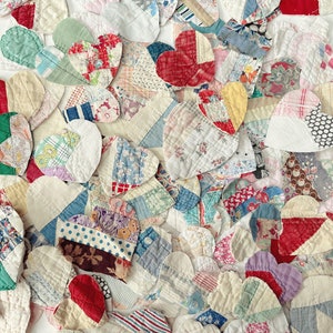 May include: A collection of heart-shaped fabric patches in various colors and patterns. The patches are made from different fabrics, including floral prints, stripes, and solid colors. The hearts are arranged closely together, creating a textured surface.