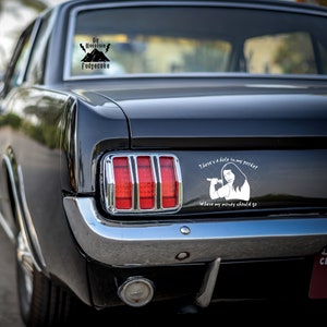 K&ouml;nnte beinhalten: Ein schwarzes Auto mit einem wei&szlig;en Aufkleber auf der R&uuml;ckseite, auf dem "There's a hole in my pocket where my money should go" steht. Der Aufkleber zeigt eine Comic-Frau, die ein Mikrofon h&auml;lt. Auf der Heckscheibe befindet sich ein weiterer Aufkleber mit der Aufschrift "Big Mountain Fudgecake".