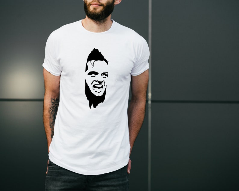 May include: White t-shirt with a black and white silhouette of a man's face with a wide smile.