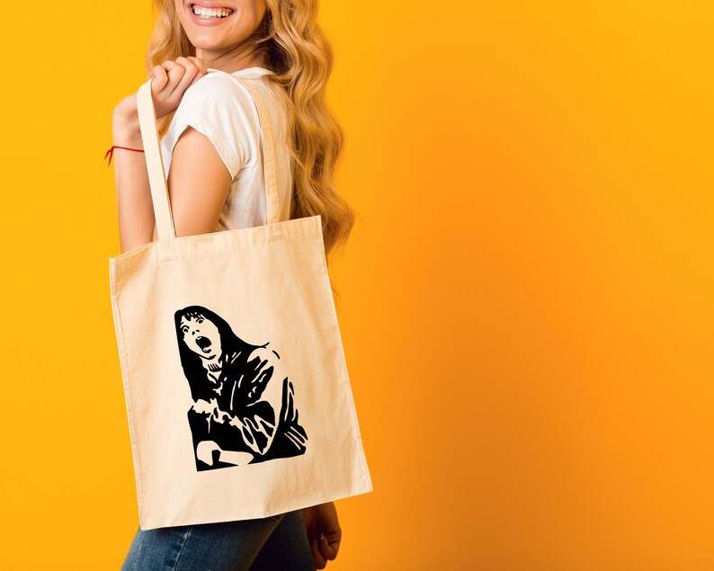 May include: A white tote bag with a black and white illustration of a woman screaming. The bag has a long handle and is being held by a person.