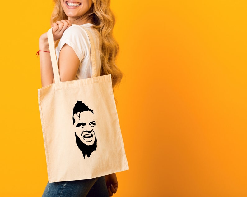 May include: A white tote bag with a black silhouette of a man's face on it. The man has a beard and is smiling.