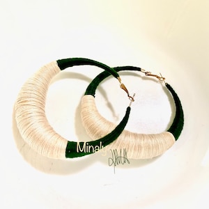 May include: A pair of large hoop earrings made of white and green yarn. The earrings are wrapped in a thick layer of white yarn and have a green velvet trim.