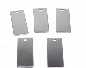 Puede incluir: Cinco etiquetas rectangulares de metal plateado con un agujero en la parte superior. Las etiquetas están en blanco y listas para ser personalizadas.