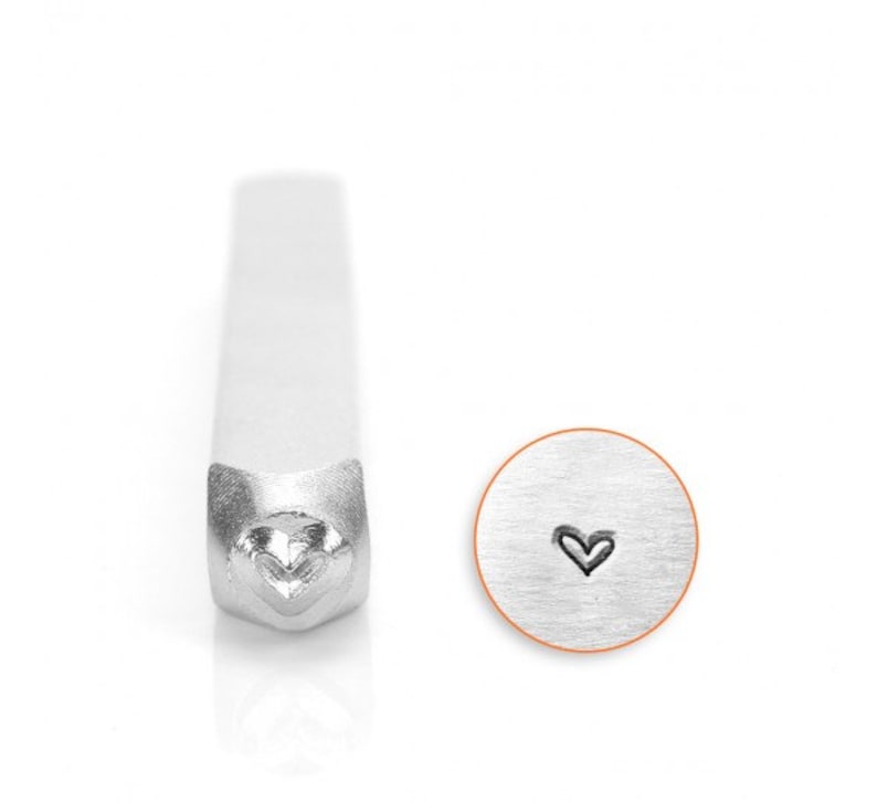 May include: A silver metal stamp with a heart design. The stamp is used to create impressions in metal.