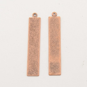 May include: Two antique copper-colored metal bar pendants with a loop at the top. The pendants are rectangular and have a distressed finish.
