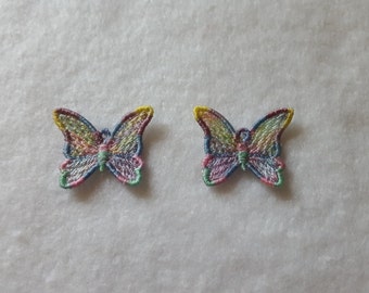 May include: Two embroidered butterfly patches. Each butterfly has wings in a rainbow of colors, including yellow, pink, blue, and green. The edges are outlined in a darker thread. The patches are on a white, textured background.