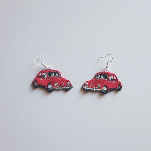 May include: A pair of red car-shaped earrings with silver hooks. The cars are detailed with white headlights and black tyres.