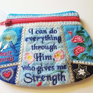Puede incluir: Una bolsa azul de tela con cremallera y diseño de patchwork. La bolsa tiene imágenes bordadas de pájaros, flores, corazones y estrellas. El texto "Puedo hacer todo a través de Él, que me da fuerza" está bordado en la bolsa.
