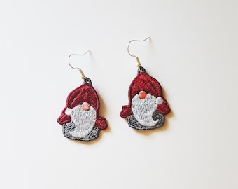 May include: A pair of dangle earrings featuring a red and white gnome design. The gnome has a red hat, a white beard, and a gray body.