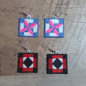 May include: Pair of earrings featuring two different quilt block designs. One pair is blue, white, and pink with a starburst pattern. The other pair is red, black, and white with a diamond pattern.