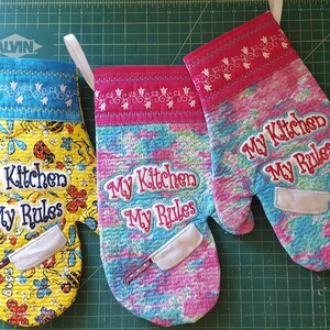 May include: Three colorful oven mitts with the text "My Kitchen My Rules" embroidered on them. Each mitt has a different pattern and color scheme: yellow with butterflies, pink with a tie-dye pattern, and blue with a floral pattern.
