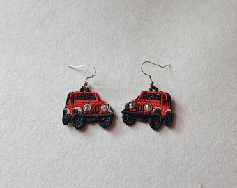 May include: A pair of embroidered earrings shaped like red and black jeeps. The earrings have silver-colored hooks and are set against a light background. The jeep details include headlights and tires.