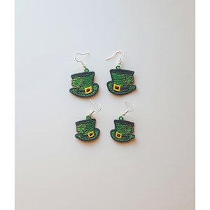 May include: Four green leprechaun hat earrings with a gold buckle and shamrock design. The earrings are on a white background.