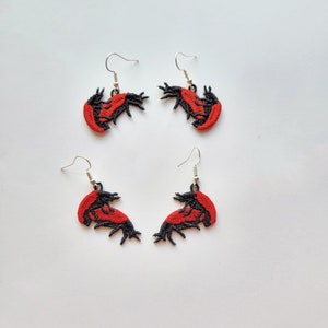 May include: A pair of red and black embroidered earrings shaped like lobsters. The earrings are hanging from silver hooks.