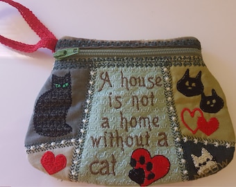 May include: A green fabric zippered pouch with a red handle. The pouch is decorated with embroidered black cats, red hearts, and the text "A house is not a home without a cat".