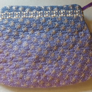 May include: A small, purple and blue fabric pouch with a white star pattern. The pouch has a drawstring closure and a purple ribbon.