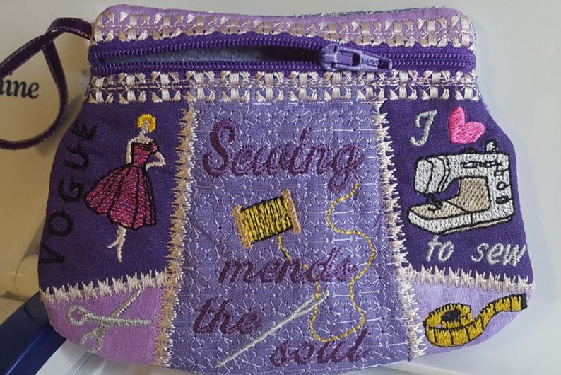 May include: Purple zippered pouch with embroidered designs. The pouch features a sewing machine, a spool of thread, scissors, a measuring tape, a woman in a dress, and the text "Vogue", "Sewing mends the soul", and "I love to sew".