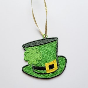 May include: Embroidered green leprechaun hat ornament with a gold ribbon for hanging. The hat features a black band with a gold buckle and a green shamrock. Perfect for St. Patrick's Day.