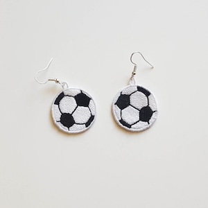 May include: A pair of silver earrings with a white and black embroidered football design.