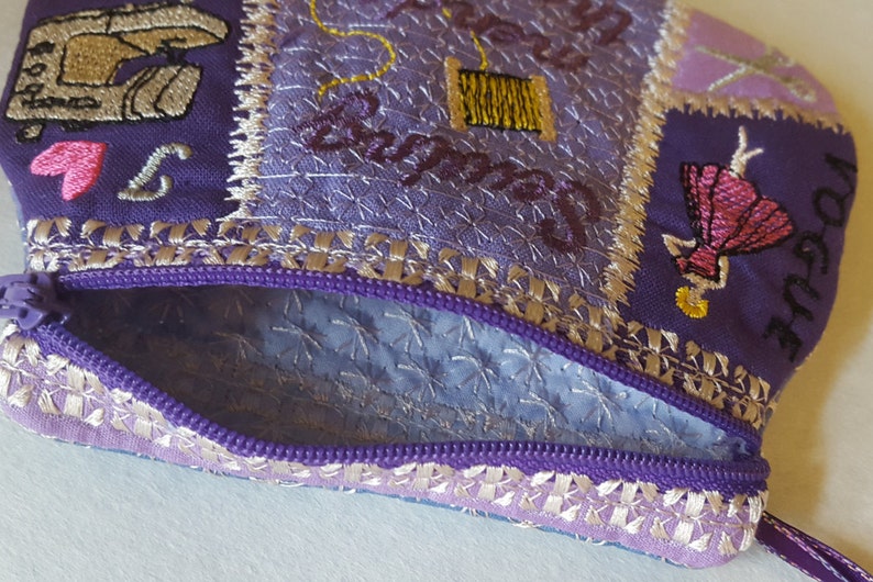 May include: Purple zippered pouch with a patchwork design featuring embroidered images of a sewing machine, a spool of thread, and a woman in a dress. The text "Sew Happy" is embroidered on the pouch.