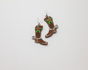 May include: A pair of brown cowboy boot earrings with a green and red star on each boot. The earrings are silver and have a hook closure.