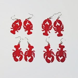 May include: Six pairs of red lobster earrings. The lobster earrings are made of metal and have a silver hook.