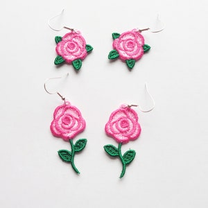 Könnte beinhalten: Ein Paar rosa und grüne gestickte Rosenohrringe. Die Ohrringe befinden sich auf einem weißen Hintergrund.