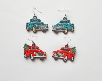 May include: A pair of earrings featuring a red truck with a Christmas tree and a teal truck. Both trucks have silver wheels and are embroidered.