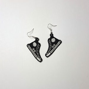 May include: A pair of black embroidered earrings shaped like high-top sneakers with white stitching and a white circle on the side.