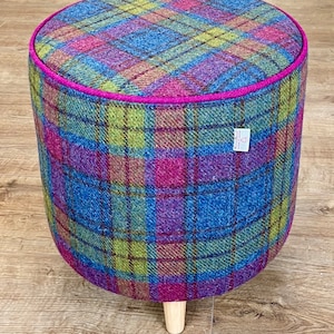 May include: A round, blue, pink and green plaid fabric footstool with a pink trim and wooden legs.