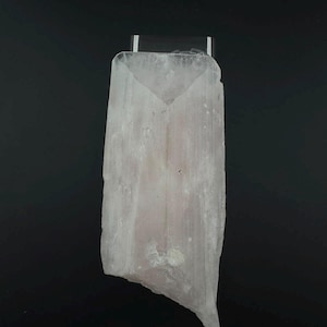 May include: A translucent, pale pinkish-white selenite crystal specimen with a vertical, fibrous, and striated texture. The crystal has a flat, rectangular top edge and tapers slightly towards a jagged, uneven base against a black background.