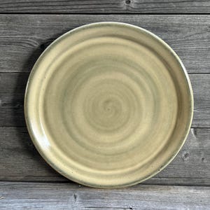 May include: A large, round, ceramic plate with a light green and yellow glaze. The glaze has a swirl pattern.