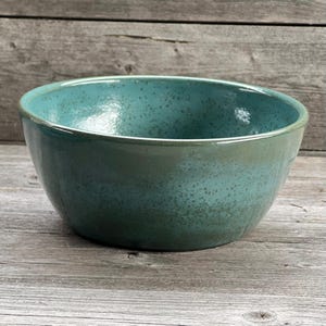May include: A large, teal ceramic bowl with a speckled glaze. The bowl is round and has a wide rim.