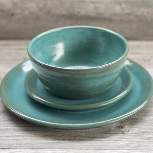 May include: A set of three teal ceramic dishes, including a bowl and two plates. The dishes have a speckled glaze and a slightly textured surface.