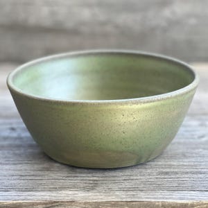 May include: A green ceramic bowl with a speckled glaze. The bowl is round and has a slight lip.
